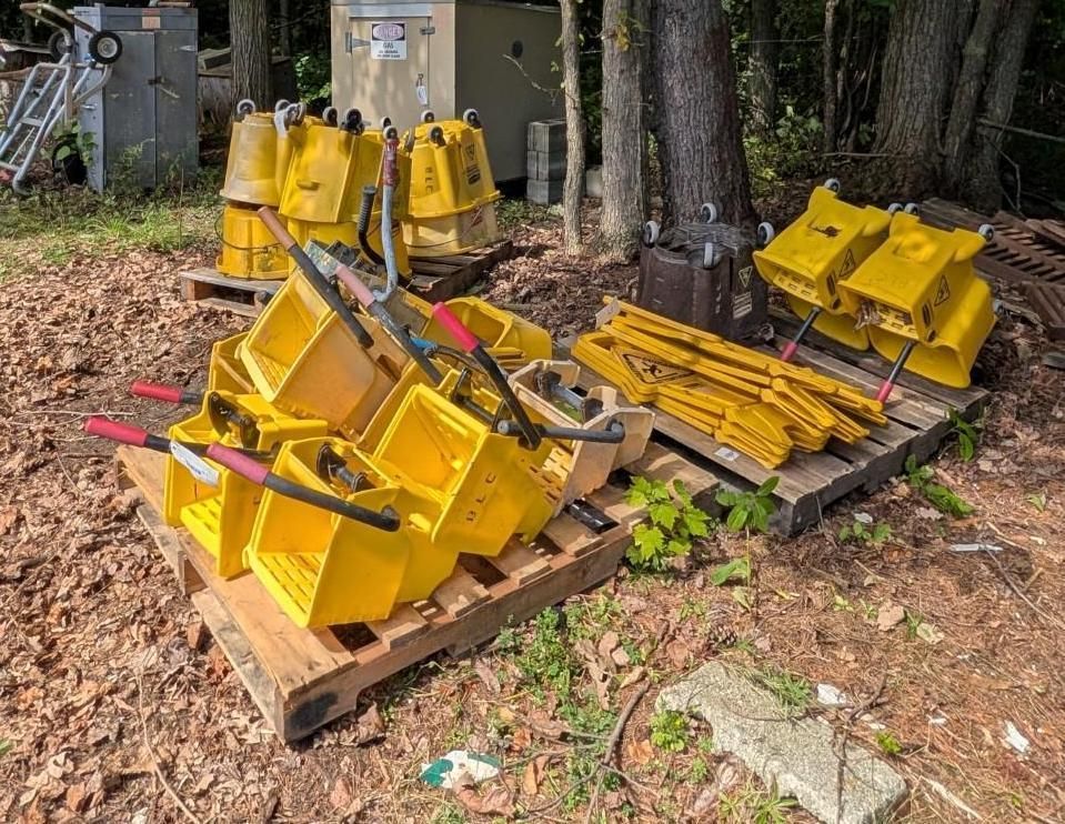 Yellow metal parts stacked on pallets outdoors beside trees and leaves