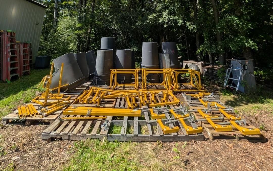 Yellow industrial metal frames and black chimneys stacked outdoors on pallets in a wooded yard
