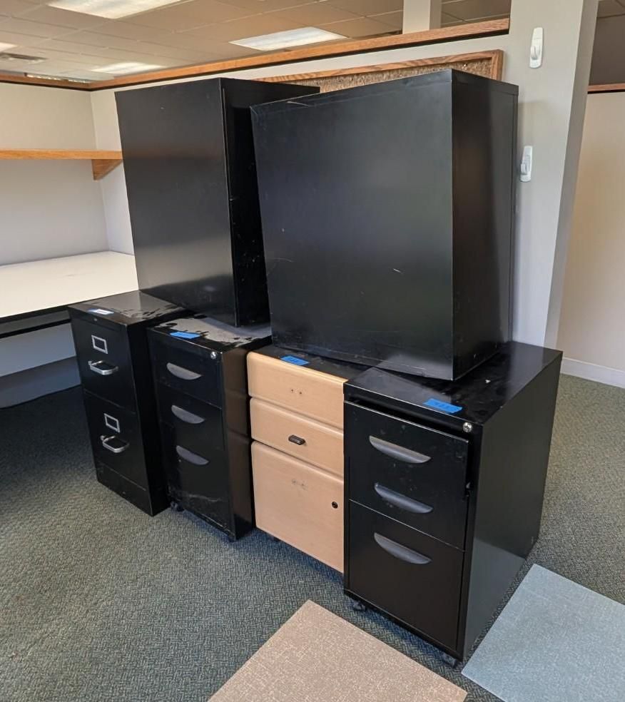 Black office desk with drawers and a large cabinet in an empty cubicle area