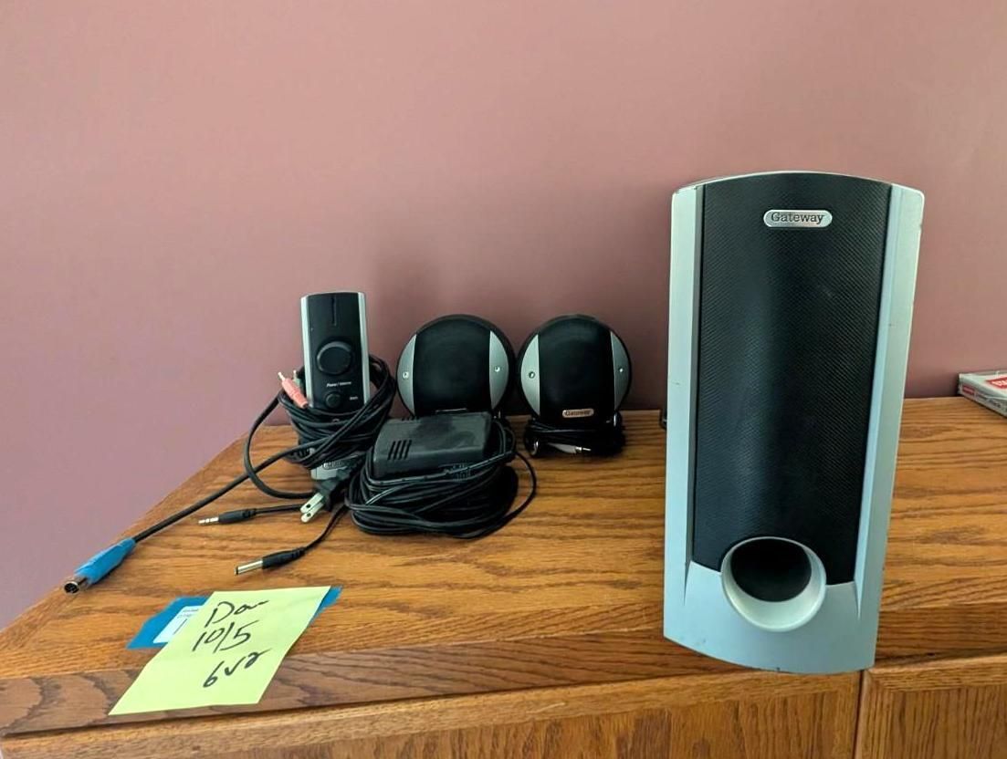 Desk with black computer speakers, tangled cables, headphones, and a small note on a wooden surface.