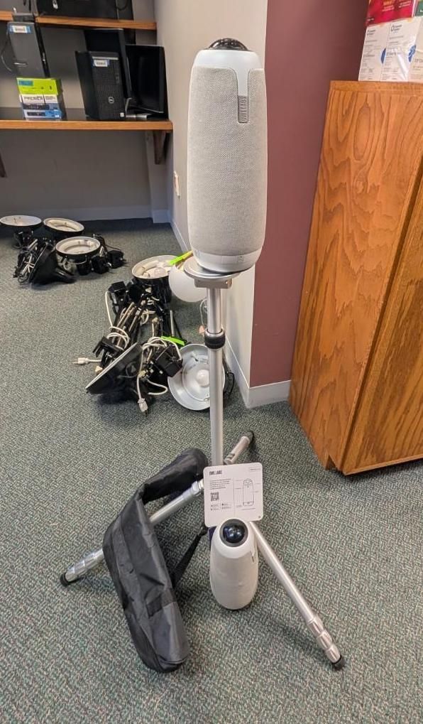 White tower fan on a tripod stand in an office corner with a black bag nearby.