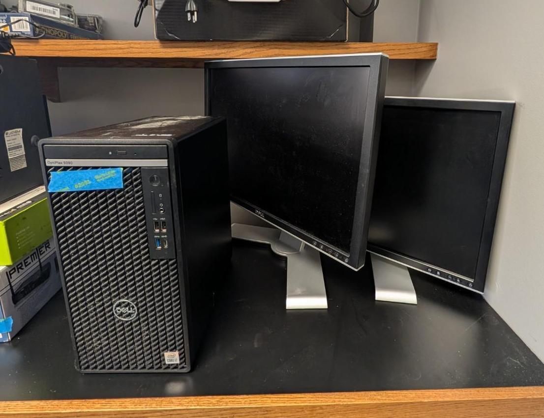 Desktop tower with two black monitors on a workbench against a shelf background