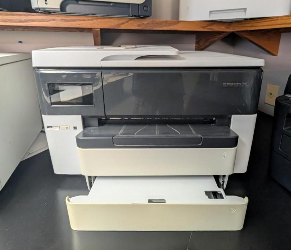 Large white multifunction printer on a desk with an extended paper tray and dark front panel