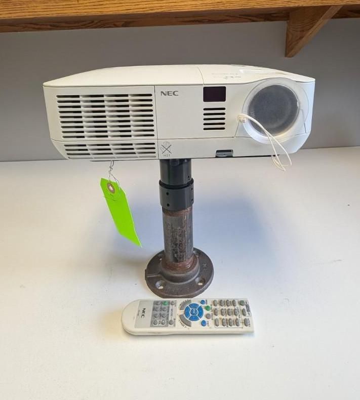 White NEC projector on a stand with a remote control below it on a desk