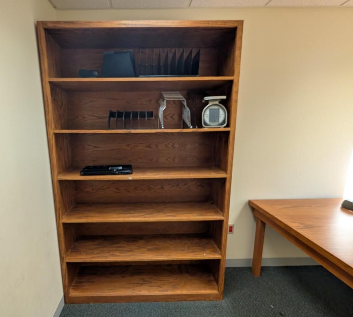 Empty wooden bookshelf beside a small wooden table in a beige room