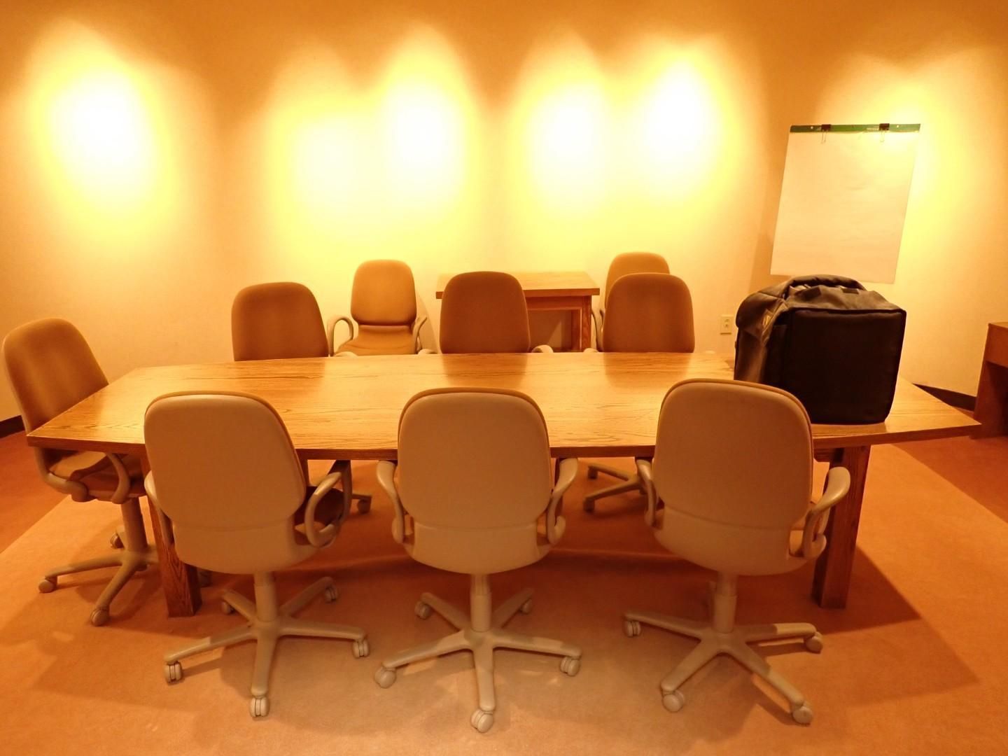 Conference room with a long table, several chairs, and a wall-mounted screen in warm lighting