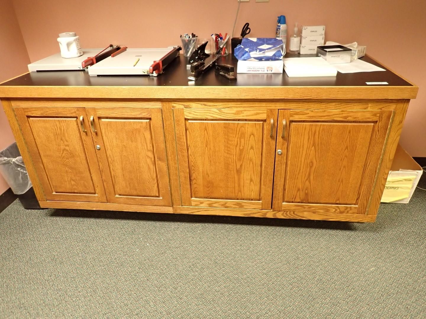 Wooden office credenza with drawers, topped with assorted office supplies and papers