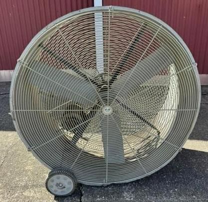 Large gray industrial fan with wheels leaning against a red wall on pavement.
