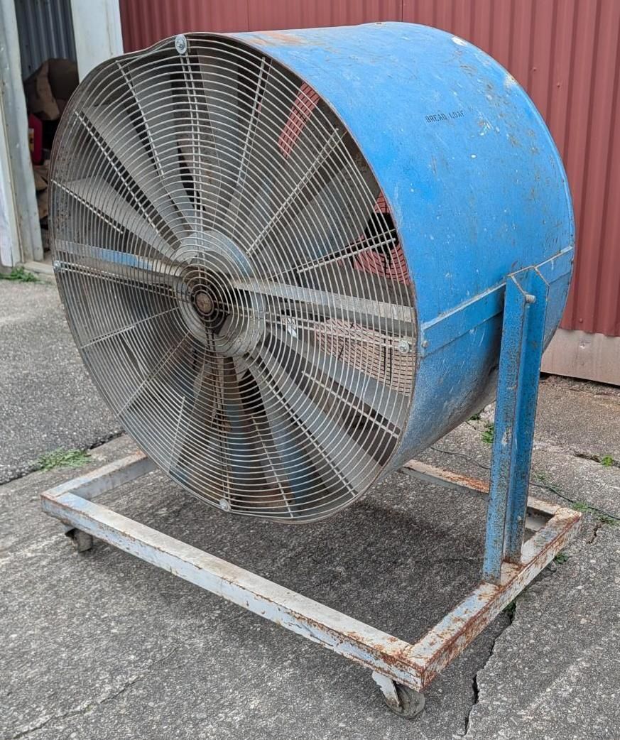 Blue industrial fan on a wheeled metal frame outdoors against a corrugated wall