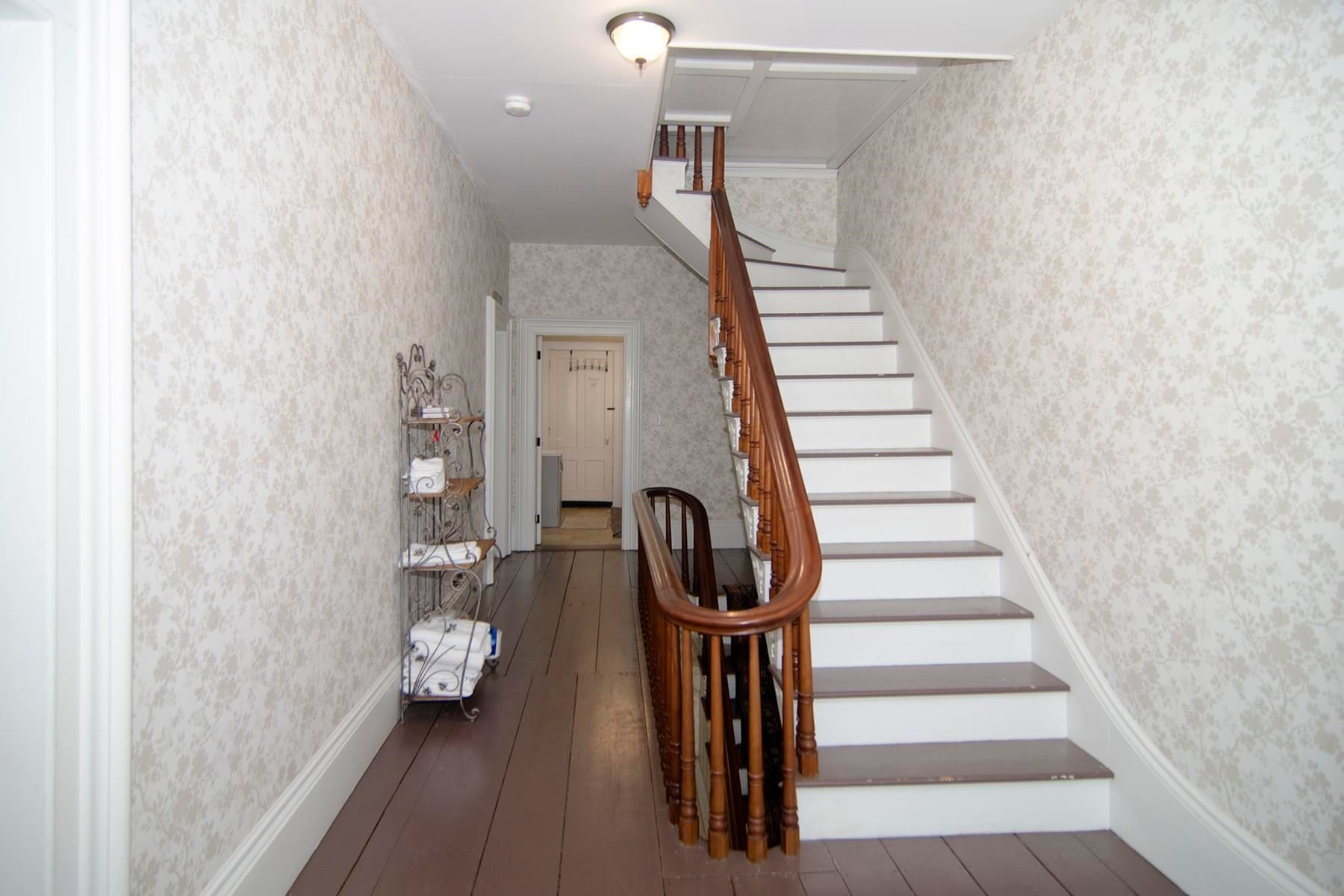 Hallway with stairs and patterned wallpaper. Brown wood floors and staircase with a wooden banister.