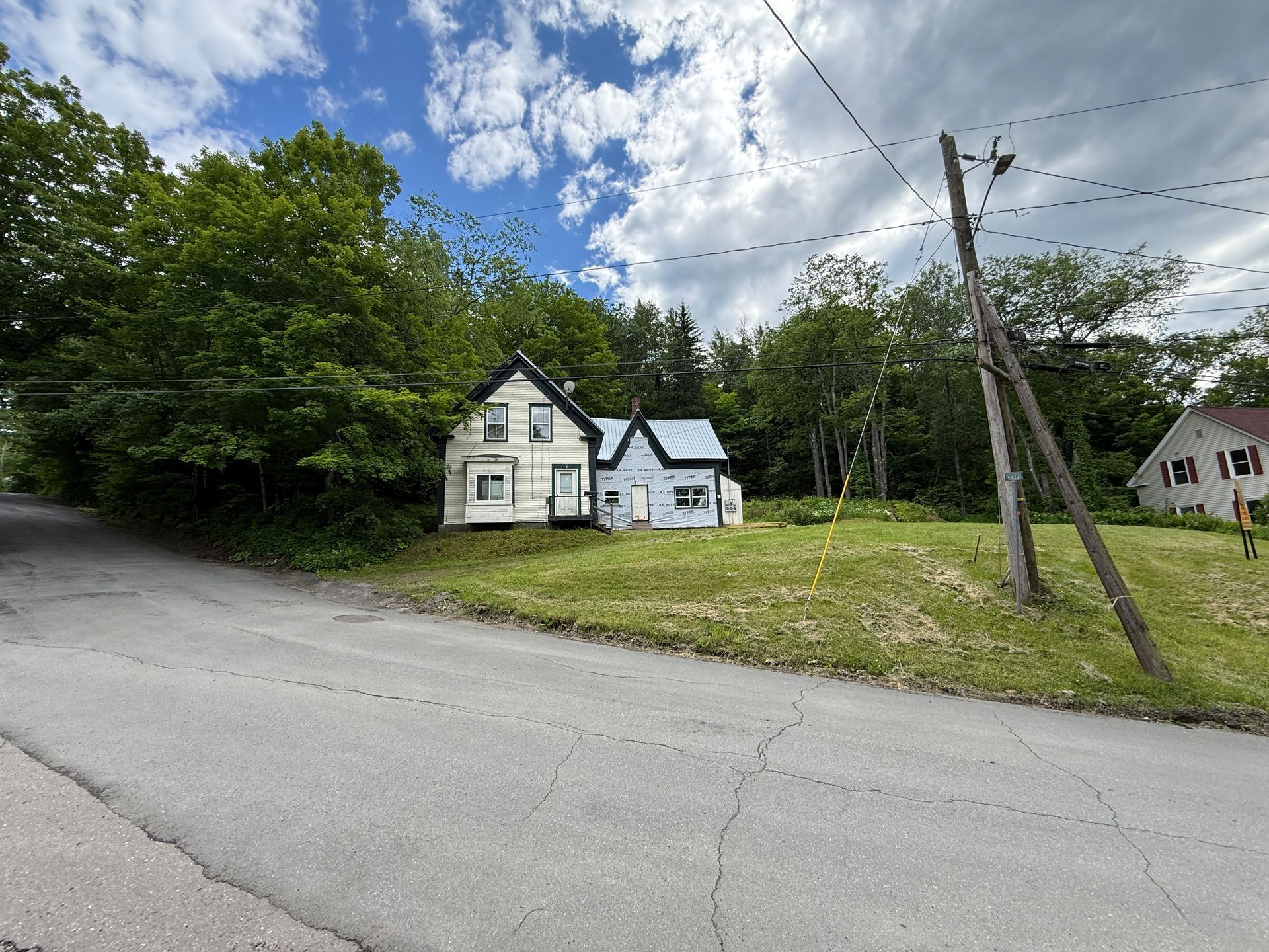 White house with dark roof beside a road, surrounded by trees under a cloudy sky