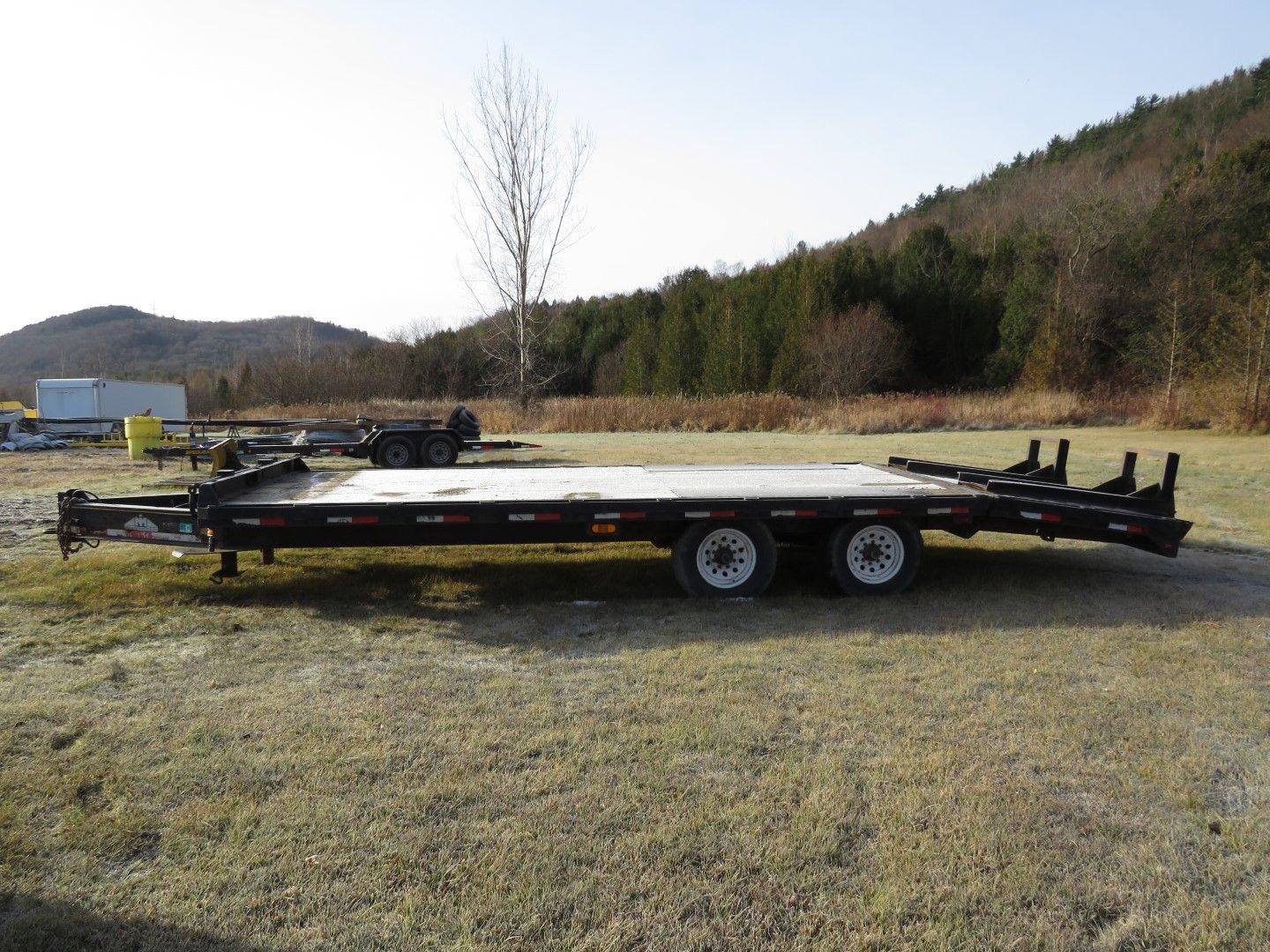 Flatbed trailer parked on grassy field with hills and trees in the background