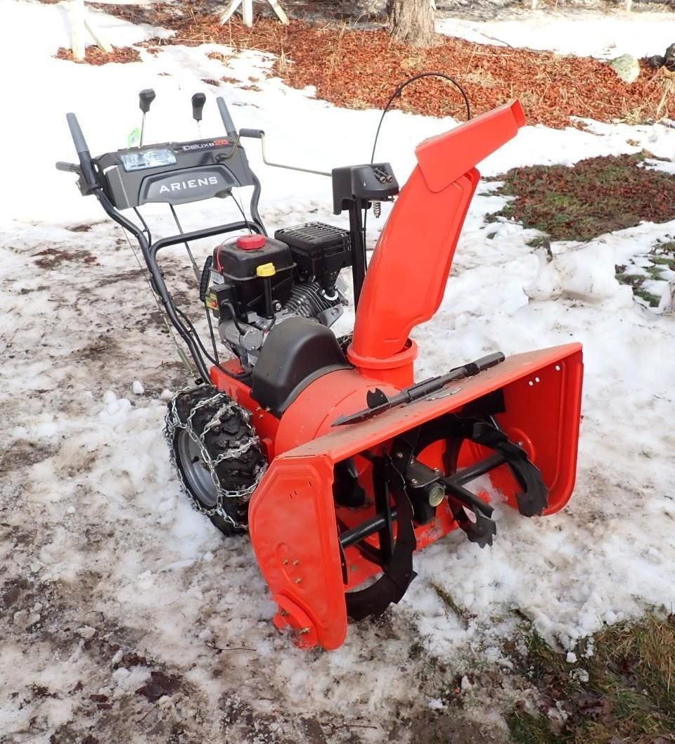 Red snow blower parked on snowy ground outdoors, with an orange chute and black engine.