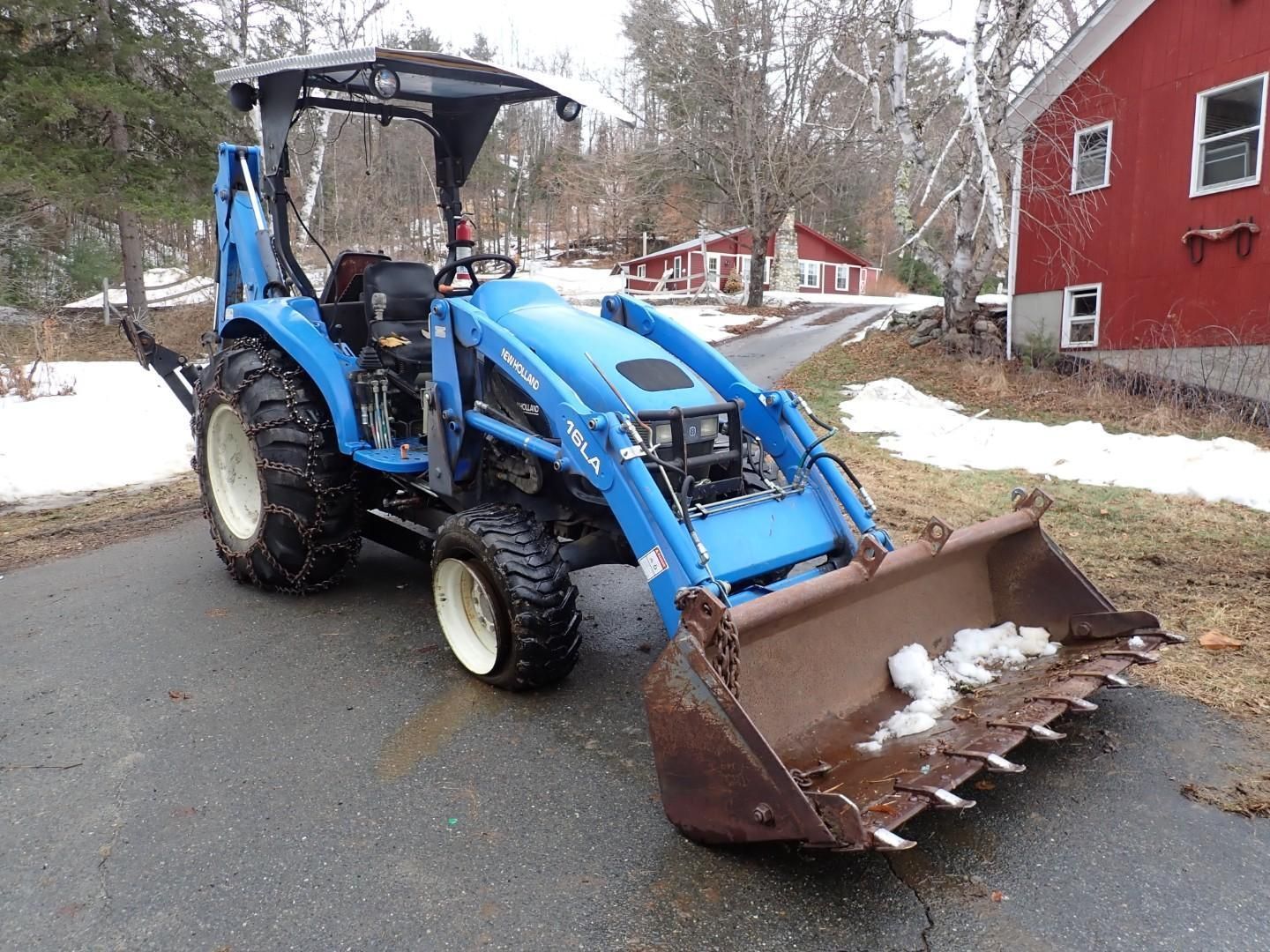 Blue tractor with front loader and bucket on a snowy residential street