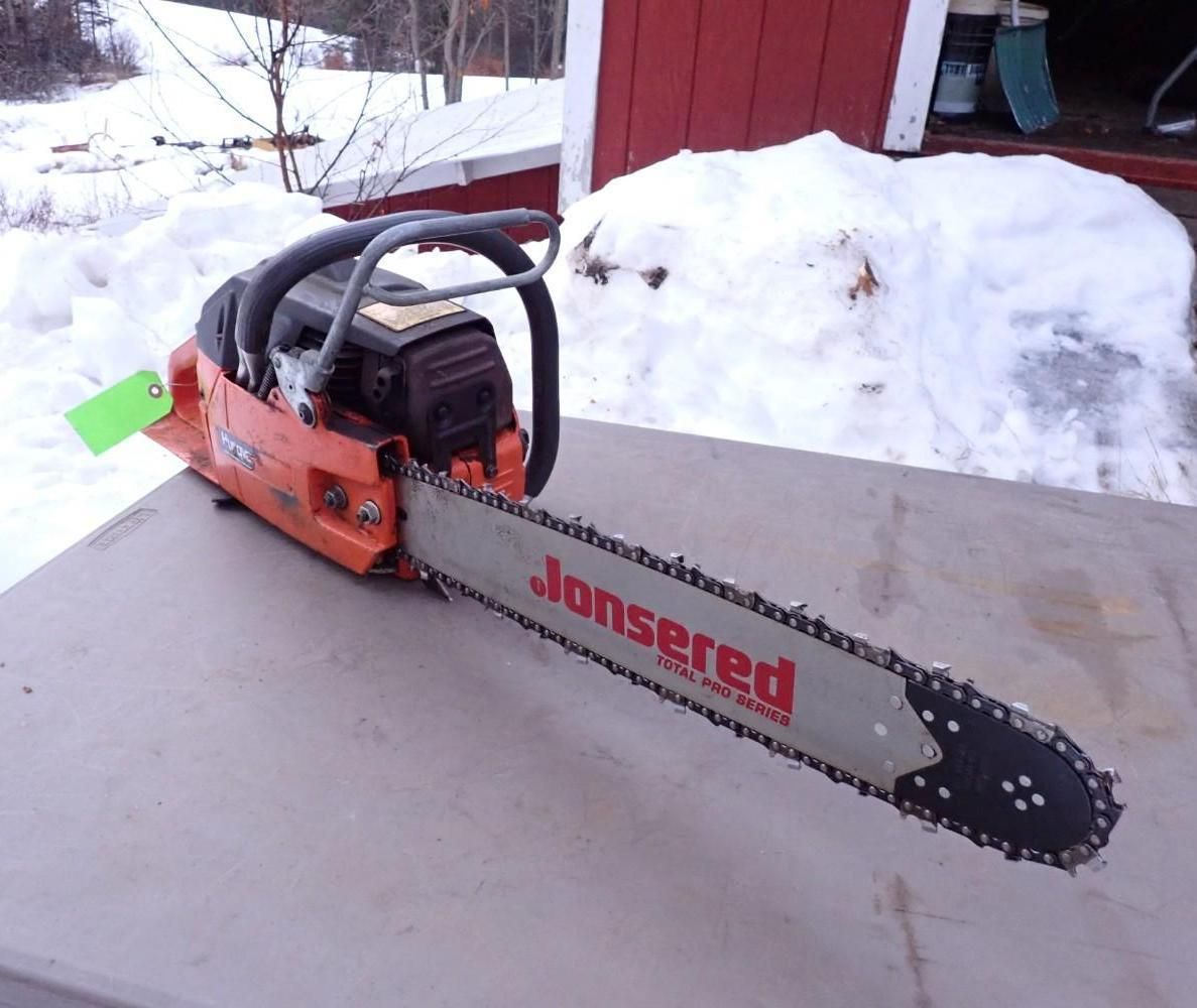 Orange chainsaw on concrete in snowy outdoor setting beside a red building