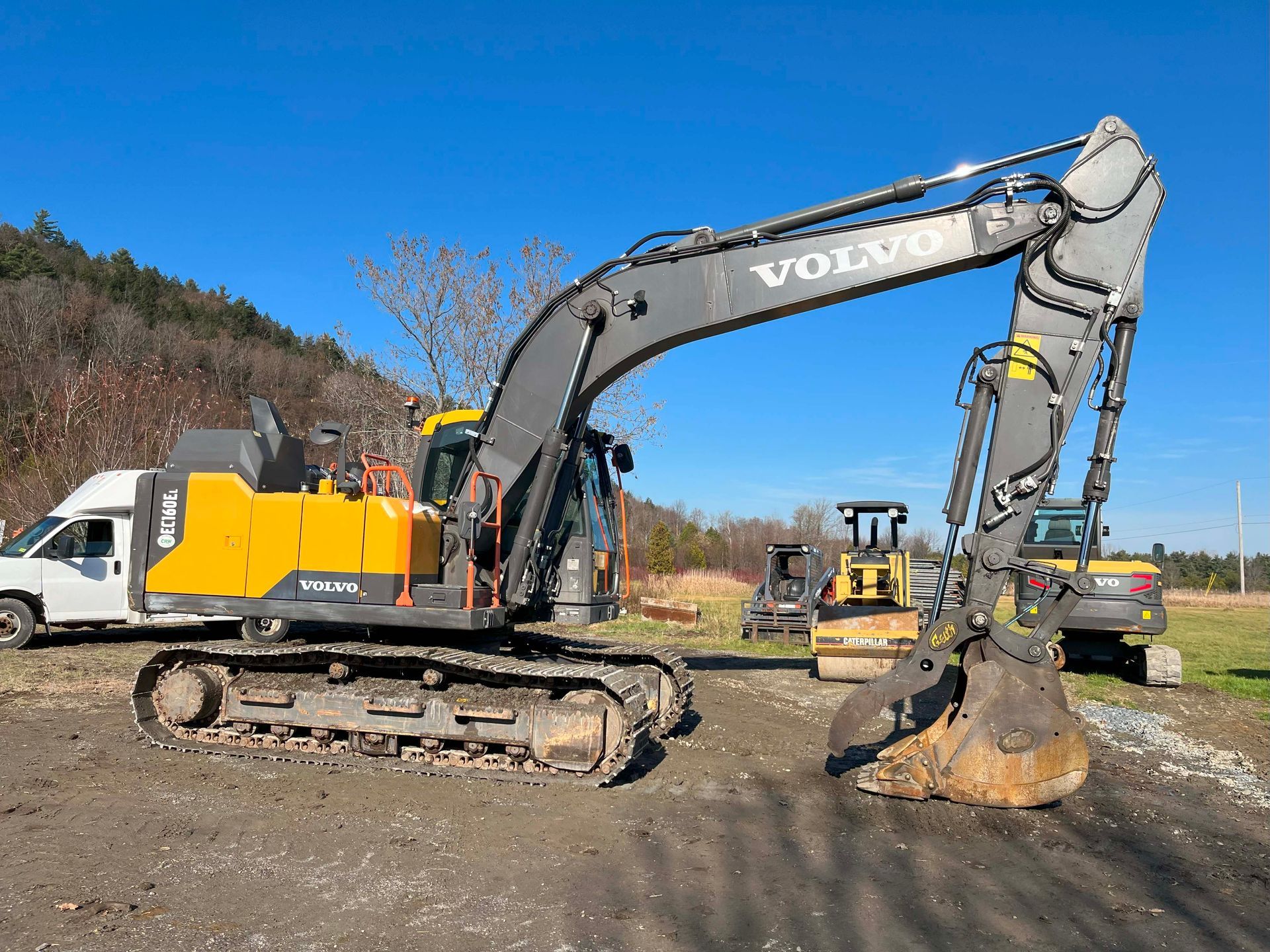 Volvo excavator on tracks lifting dirt at a construction site under a blue sky