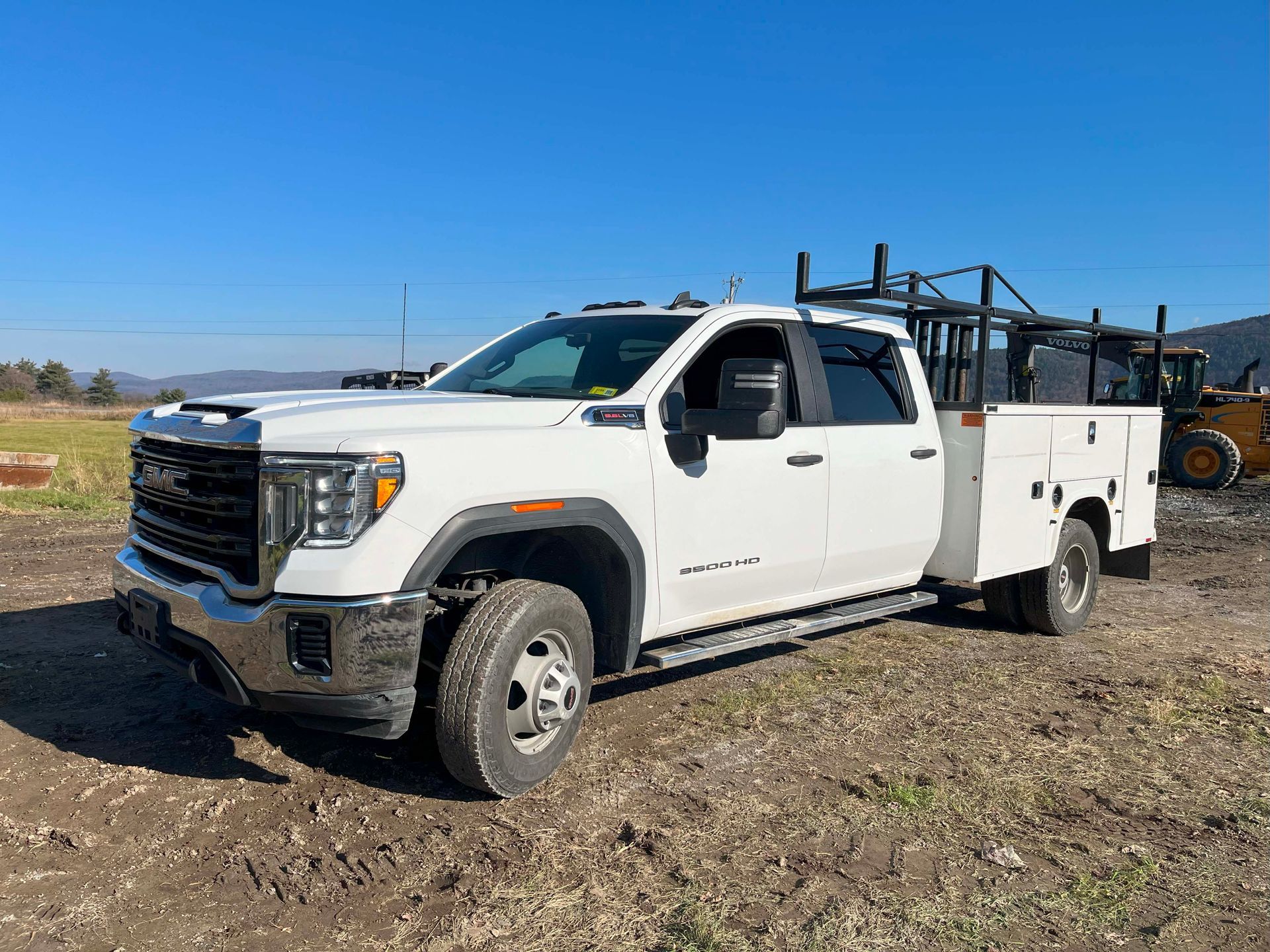 White utility truck with service bed parked on a dirt field under a clear blue sky