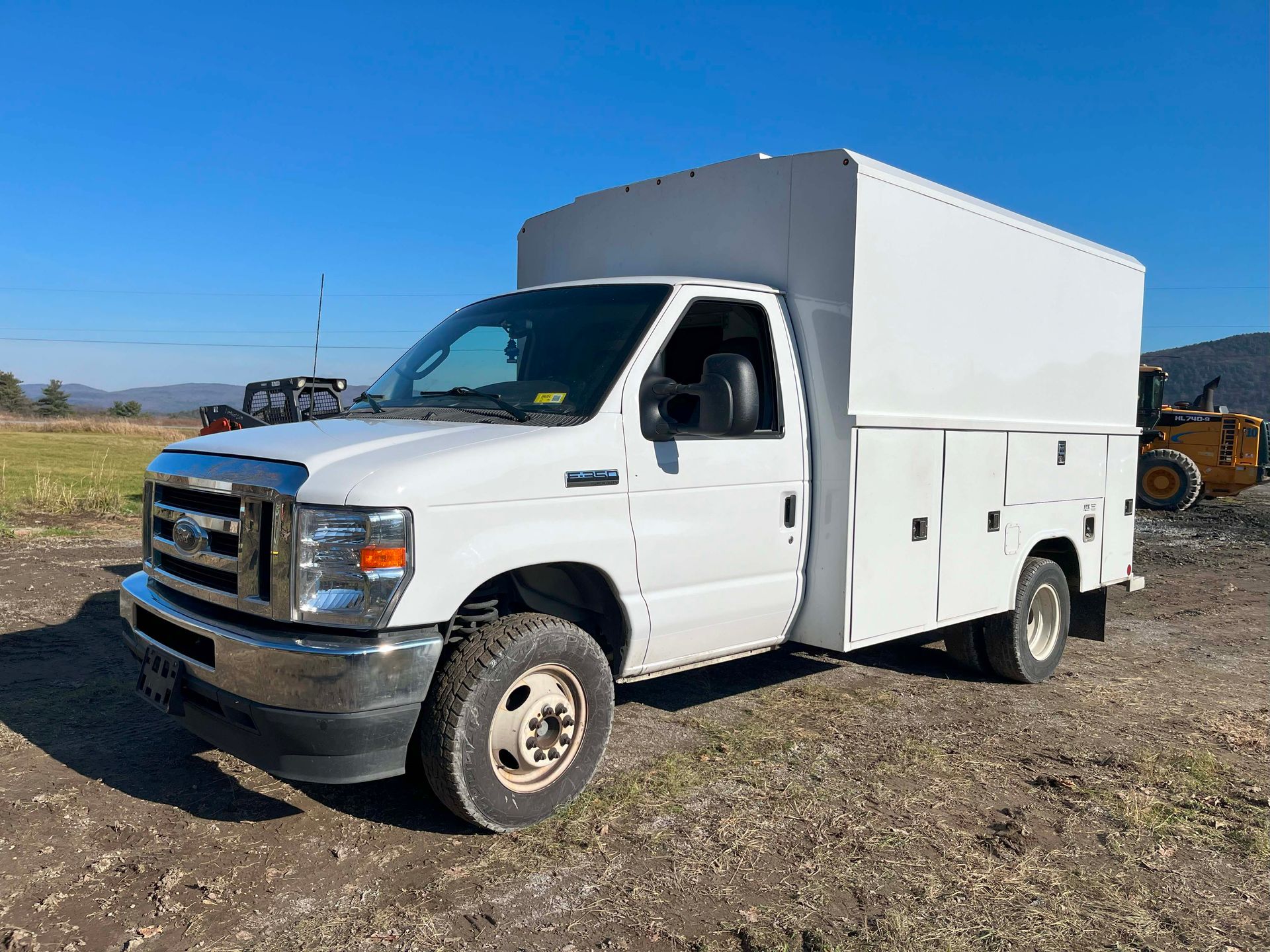 White utility truck parked on gravel under a clear blue sky, side view in an open field.