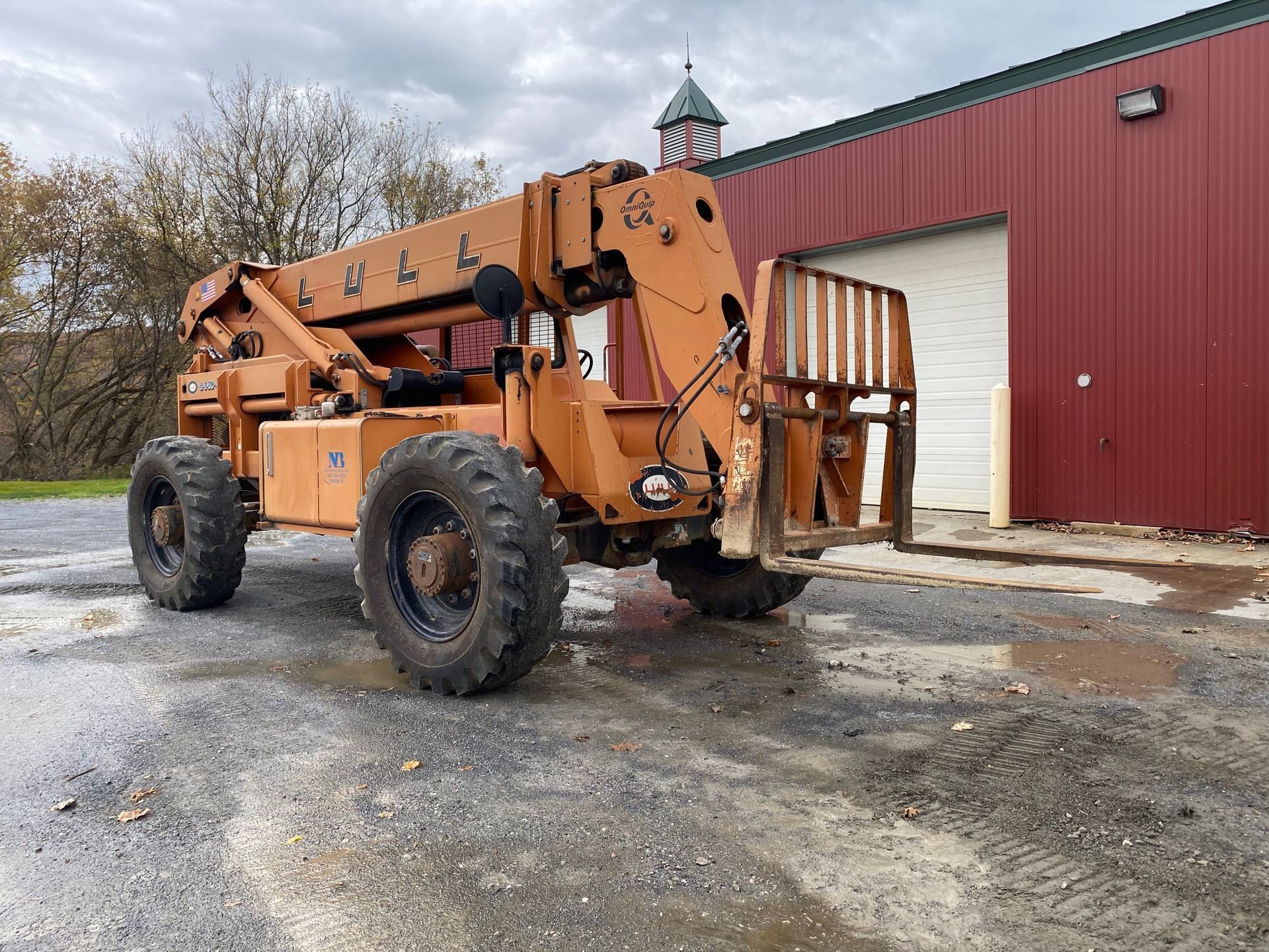 Orange forklift parked on gravel beside a red metal building on an overcast day