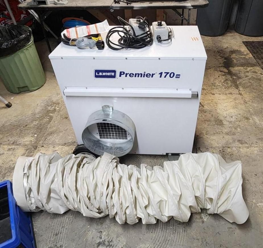 White furnace/air unit in a garage with coiled ducting on top and a large white vent hose in front.