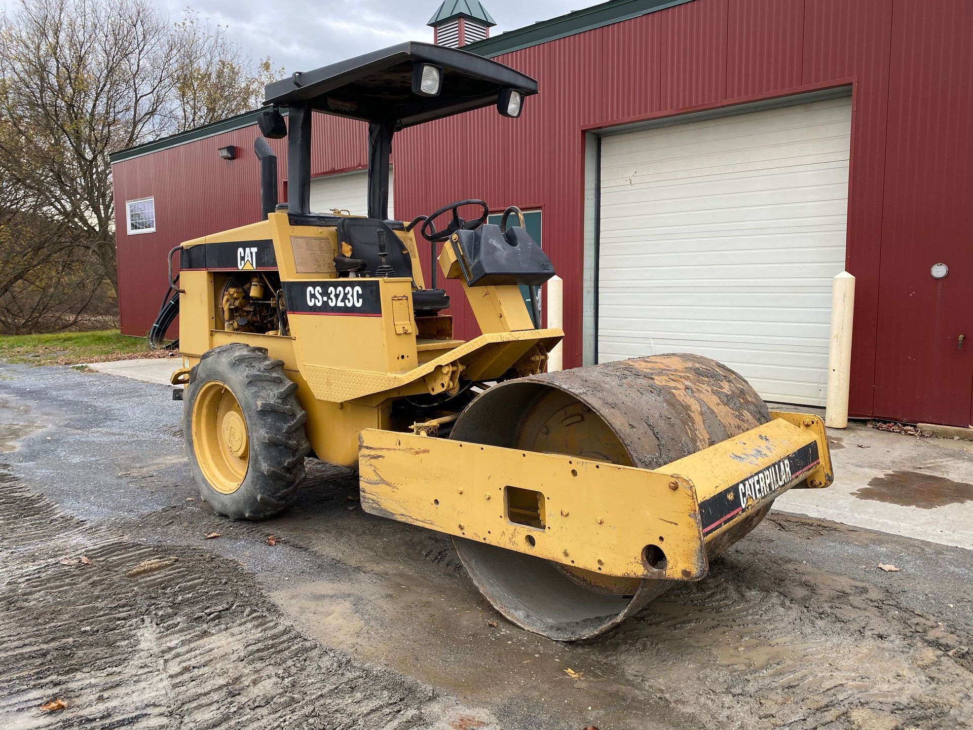 Yellow road roller parked outside a red garage
