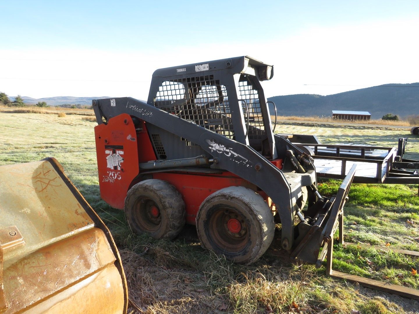 Red skid steer loader on a grassy field