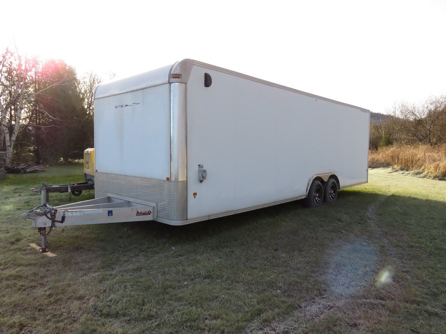 White enclosed cargo trailer parked on grass in a sunny field