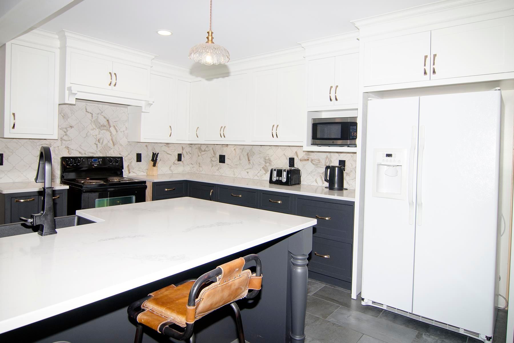 Modern kitchen with white and dark gray cabinets, island, stainless steel appliances.