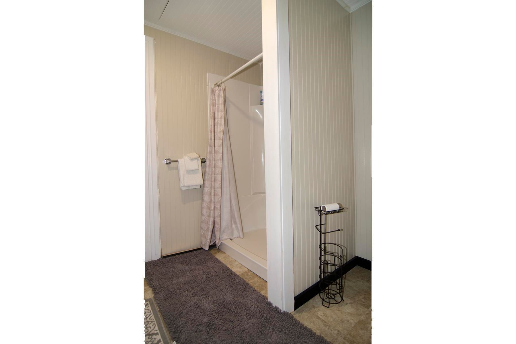 Bathroom with a shower, floral curtain, and a rug.