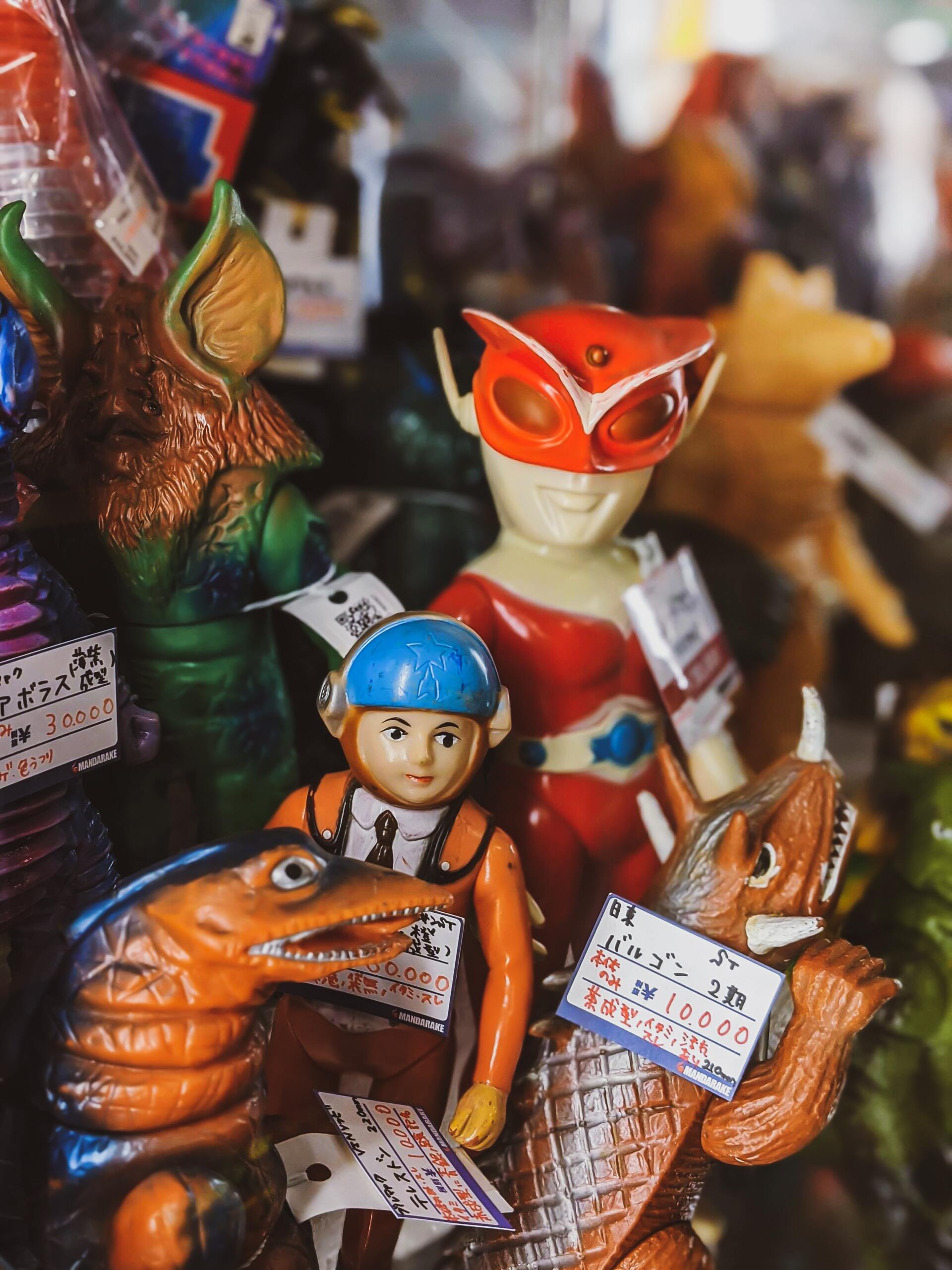 Vintage toys with price tags. Colorful creatures and a costumed figure are on display.