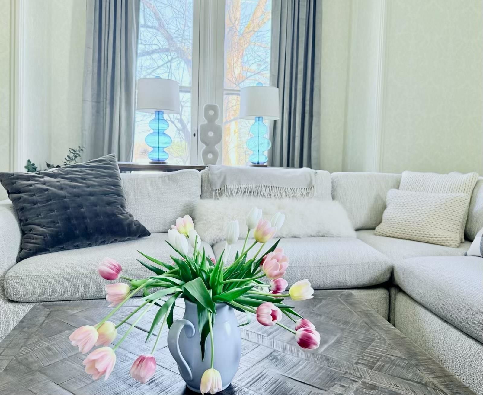 Living room with a large cream-colored sectional sofa, tulip bouquet on coffee table, and blue lamps.
