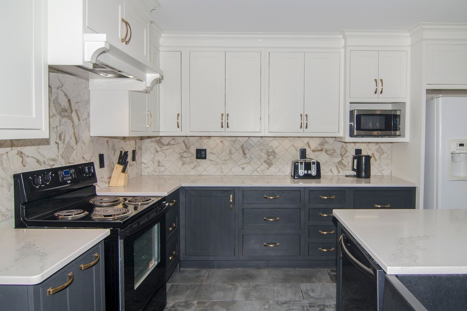 Modern kitchen with white and dark gray cabinets, marble backsplash, and white countertops.