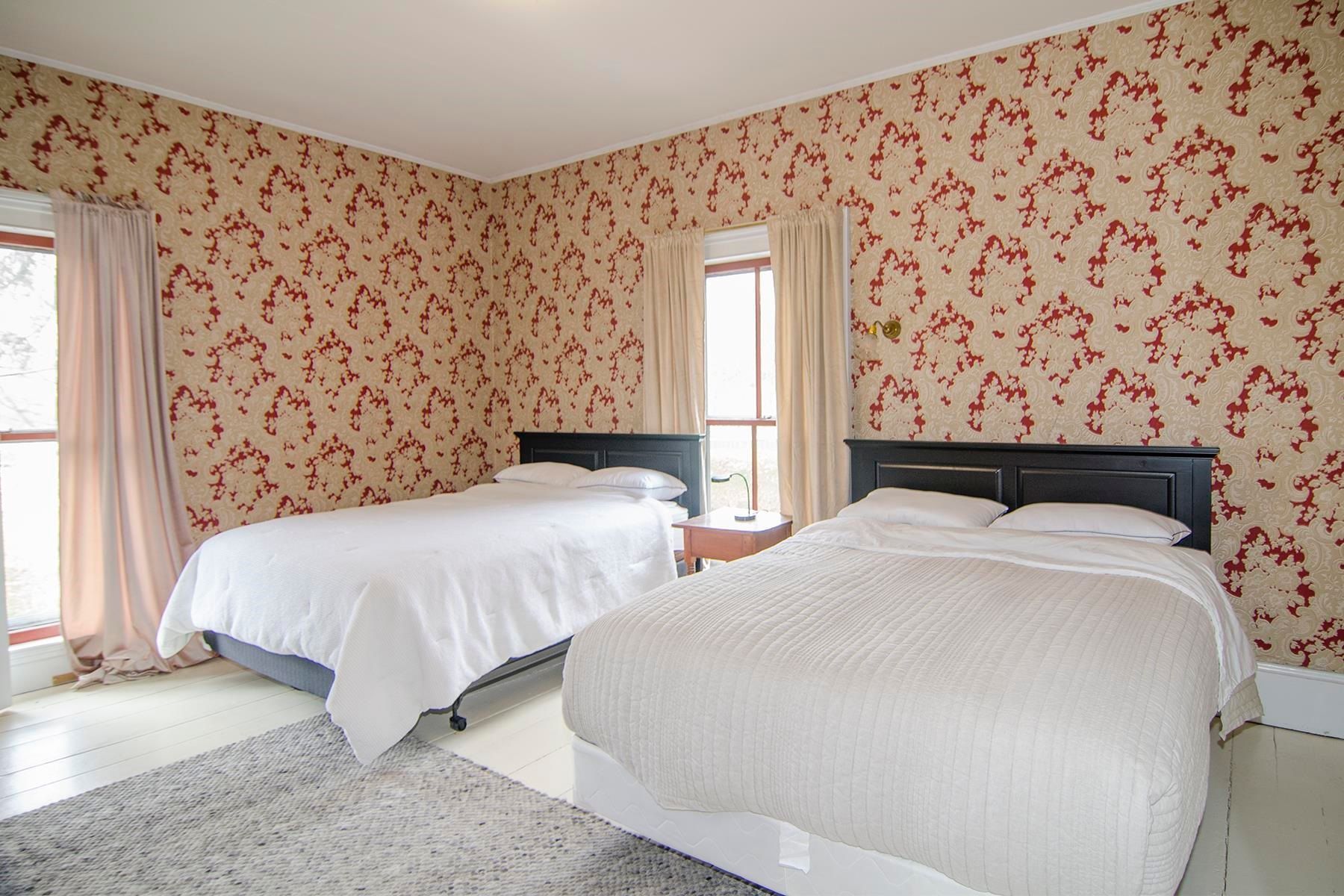 Bedroom with two beds, patterned wallpaper, curtains, and a rug.