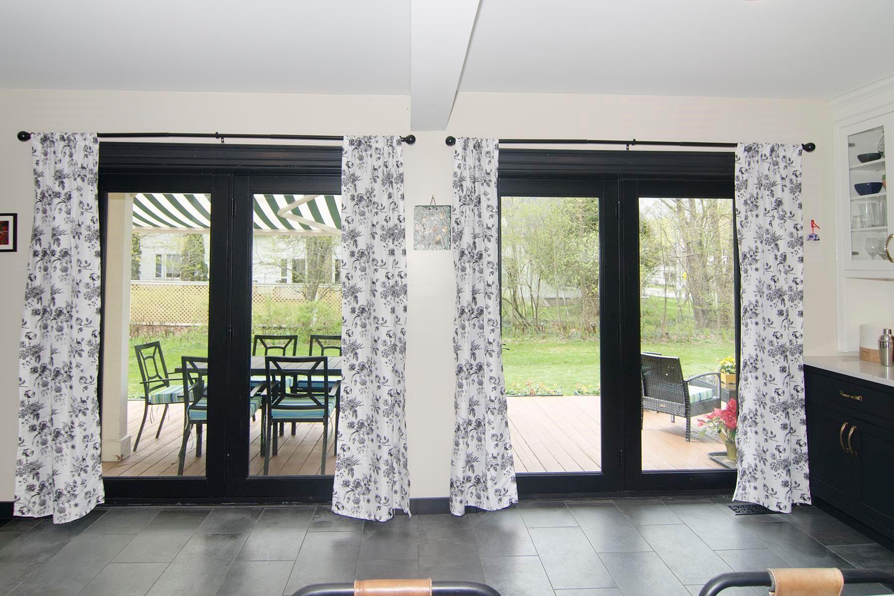 Black framed glass doors with floral curtains open to a backyard.