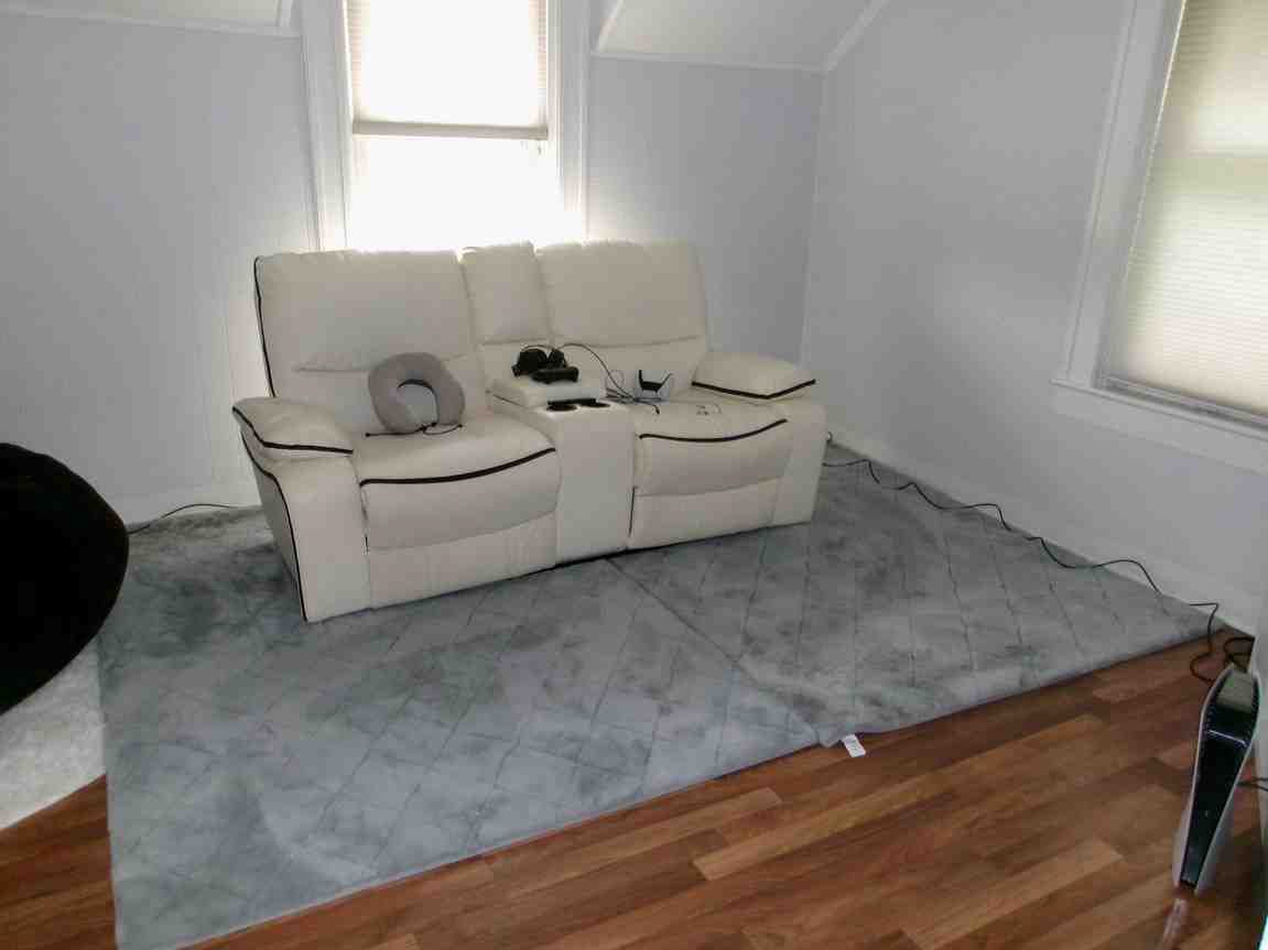 White loveseat and gray rug in a furnished room with a window and wood floor.