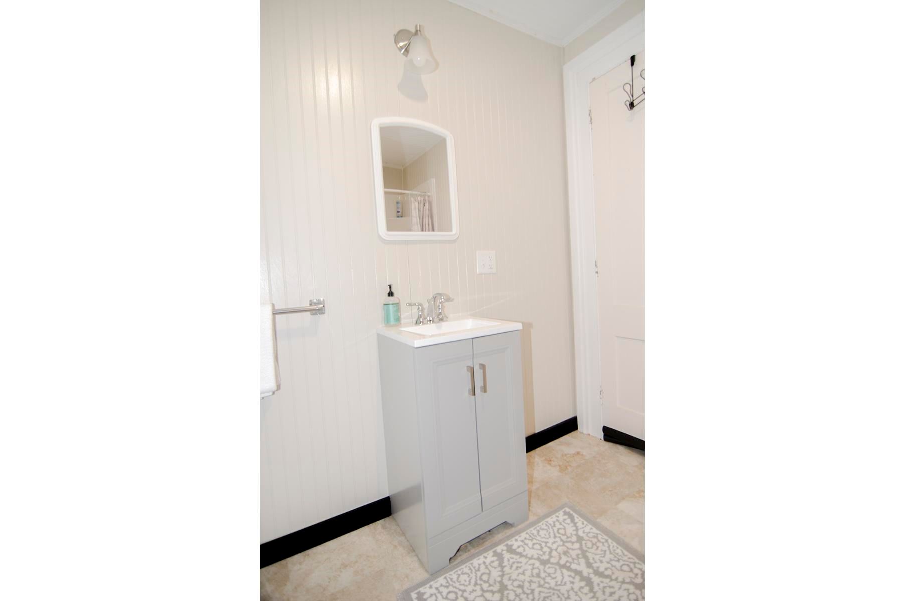 Bathroom with a white vanity, mirror, and light fixture; tan and white patterned rug.