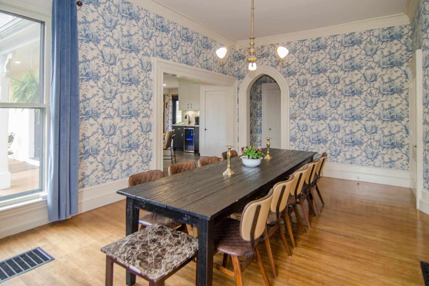 Dining room with blue patterned wallpaper, long dark table, and chairs.