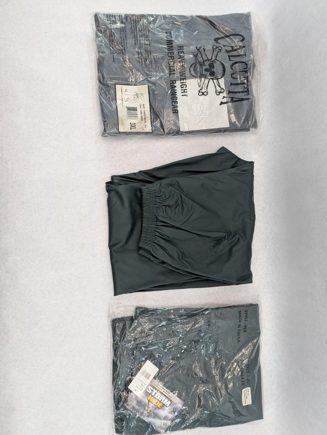 Three dark gray folded clothing items arranged vertically on a light wall.