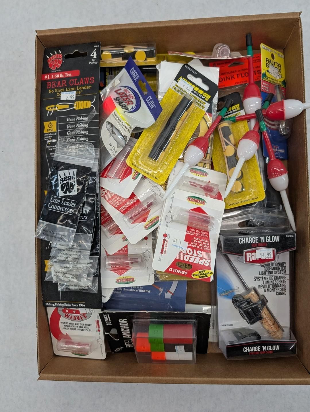 Cardboard box filled with assorted fishing tools, adhesives, and hardware supplies in red, black, yellow, and white.
