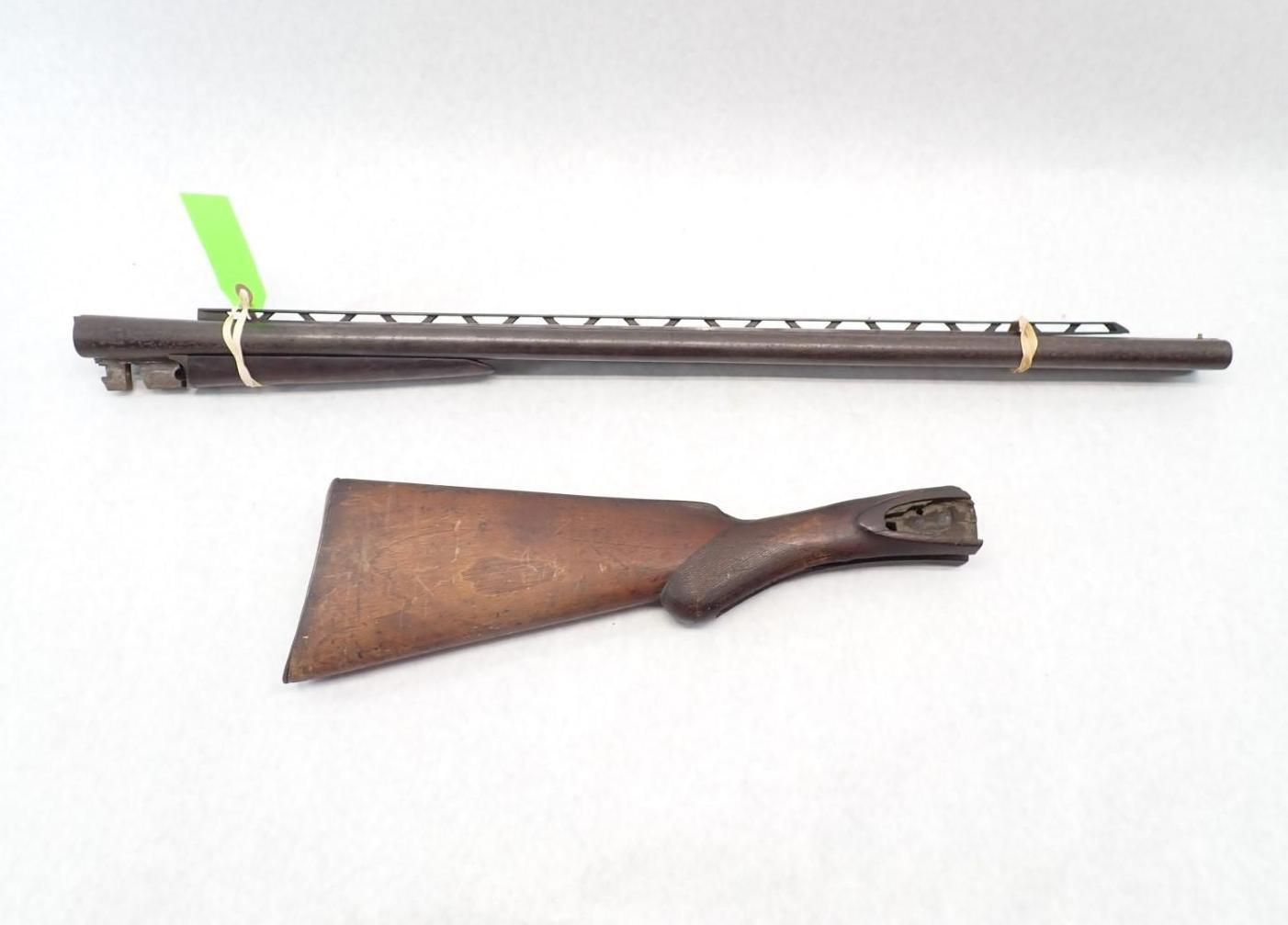 Two antique firearm parts: a long metal barrel and a wooden stock laid separately on a white background