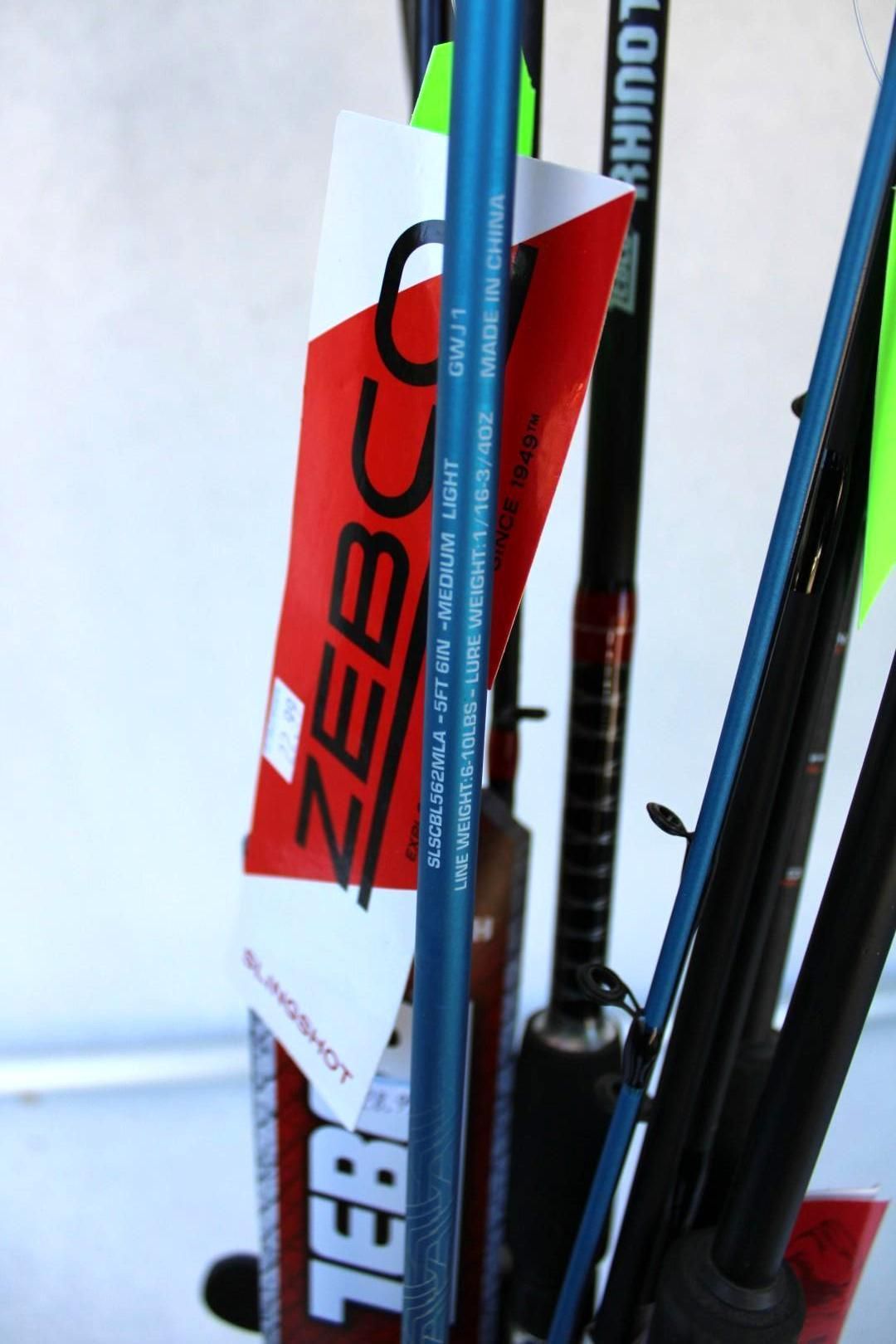 Close-up of red and black fishing poles with branded tags, standing upright against a light background