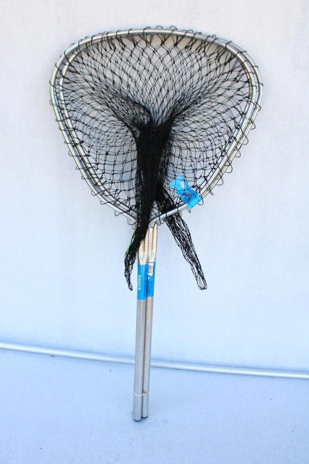 Wire-mesh scoop net with a blue handle leaning against a white wall