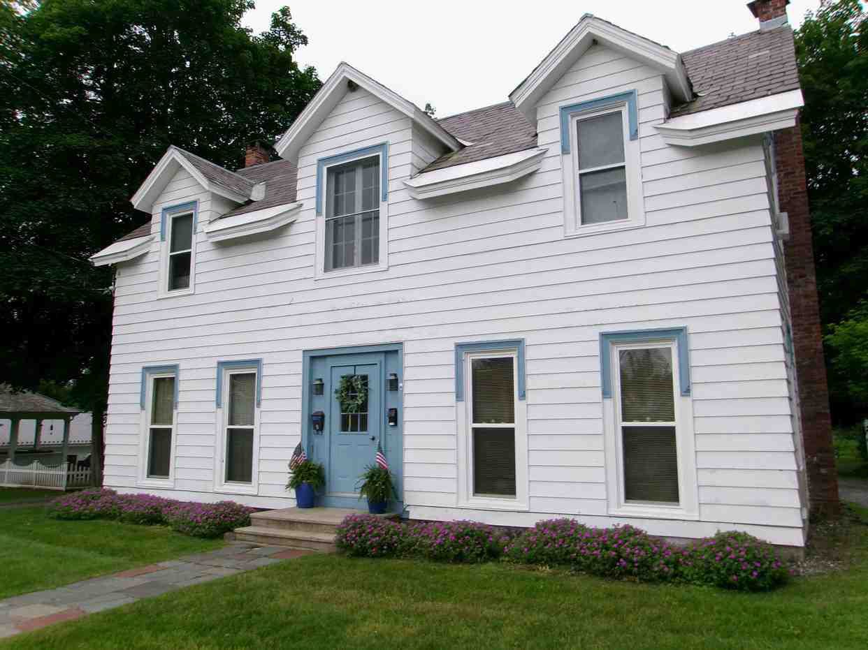 White two-story house with blue trim and front door, on a lawn with trees nearby
