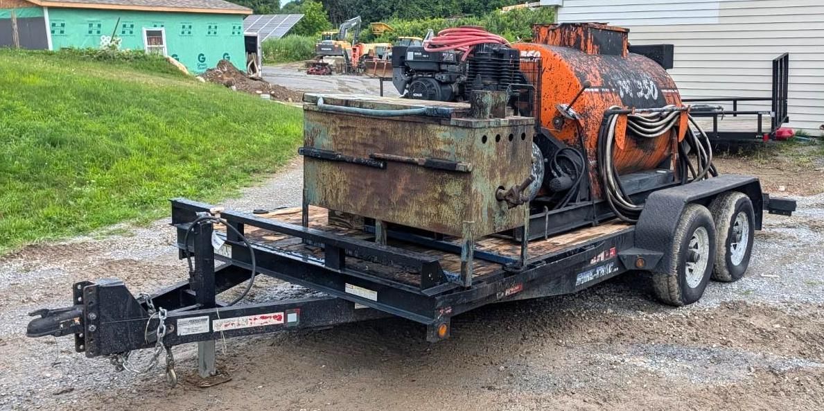 Flatbed trailer hauling a large machine beside a gravel road and grassy field