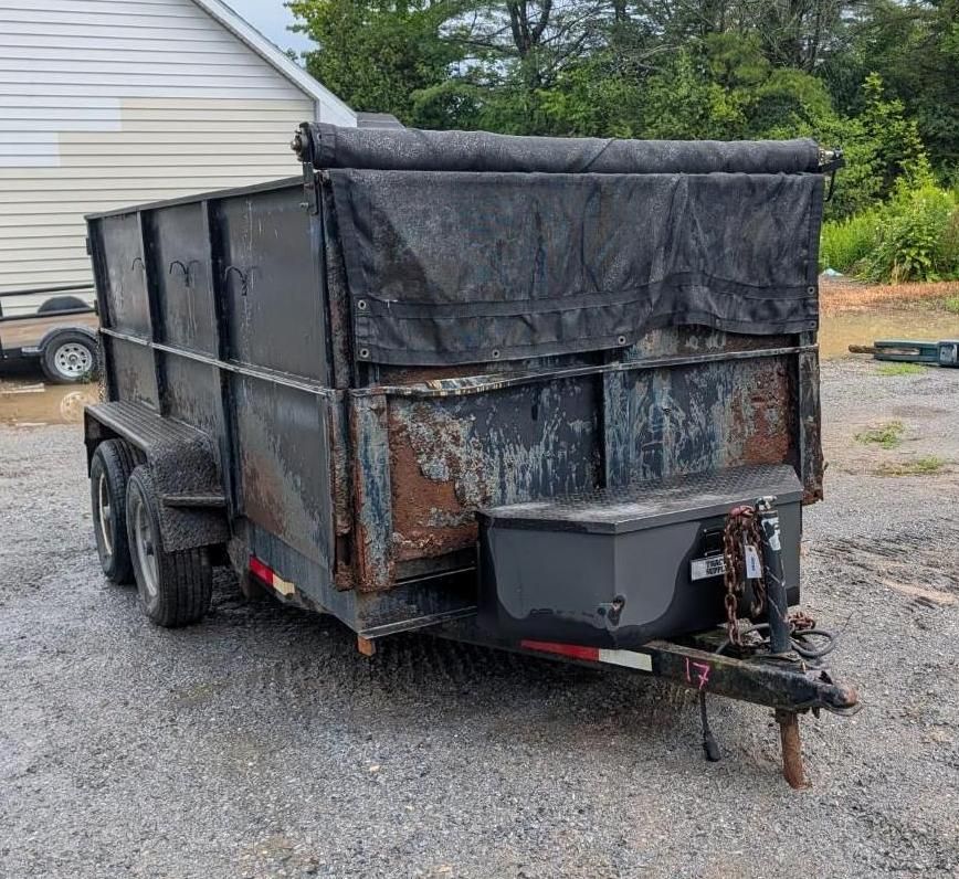 Black enclosed utility trailer with rear gate and tarp cover parked on gravel outdoors