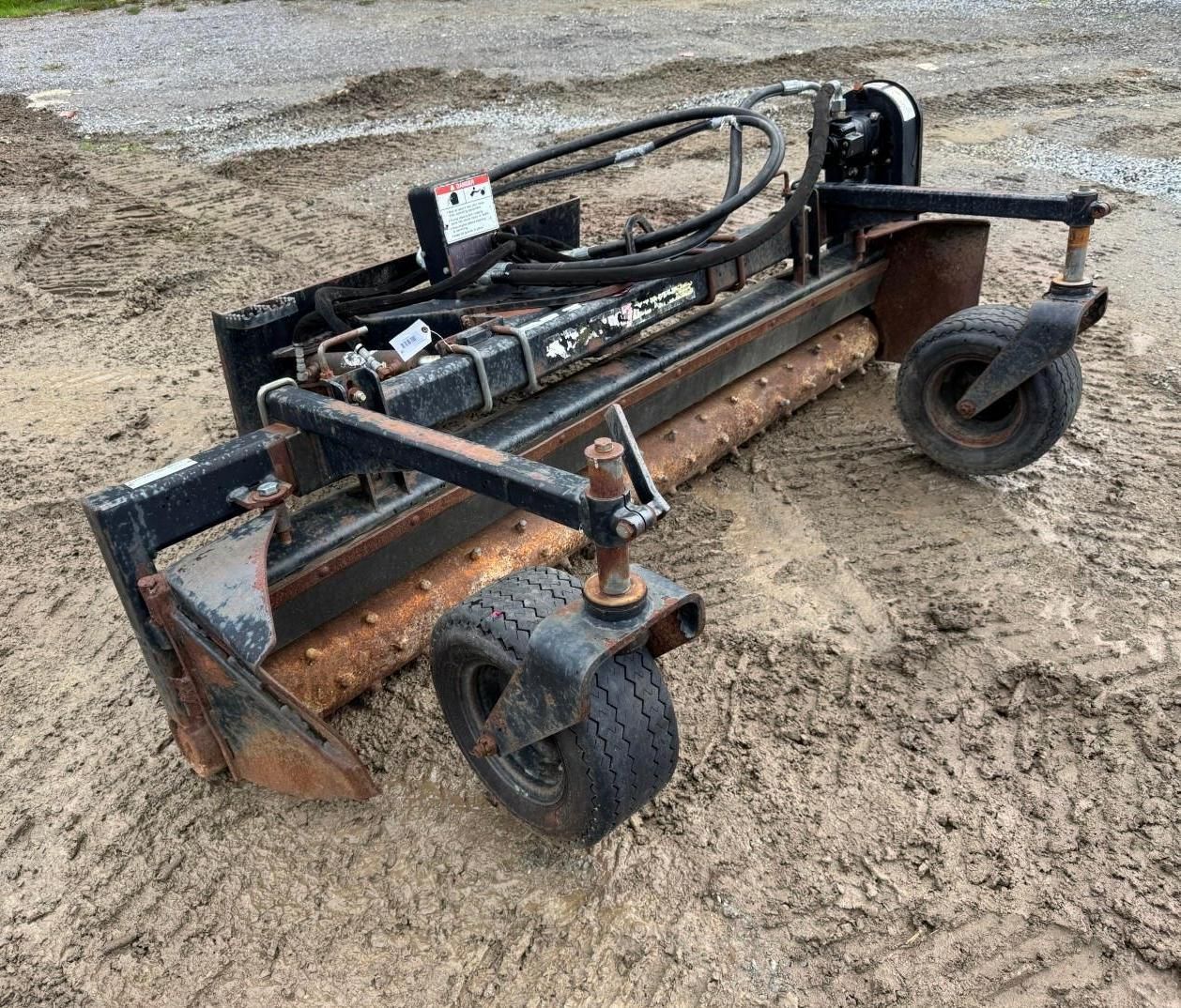 skid-steer attachment with wheels on gravel, showing a front-mounted blade or snow pusher.