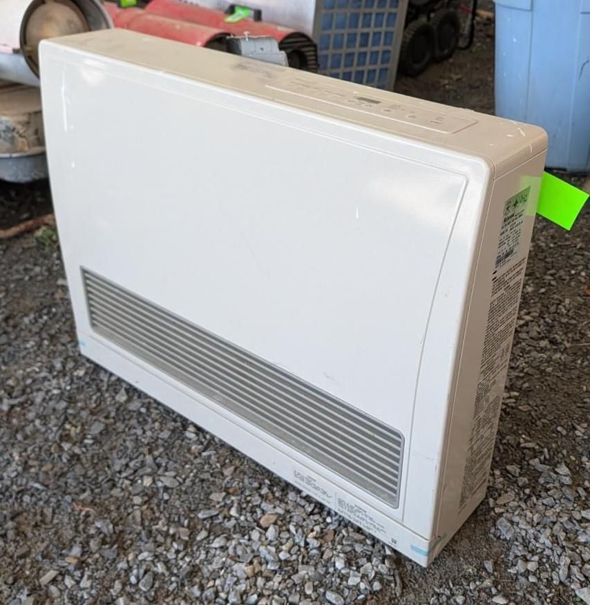 White wall-mounted heater leaning on gravel in an outdoor storage area.