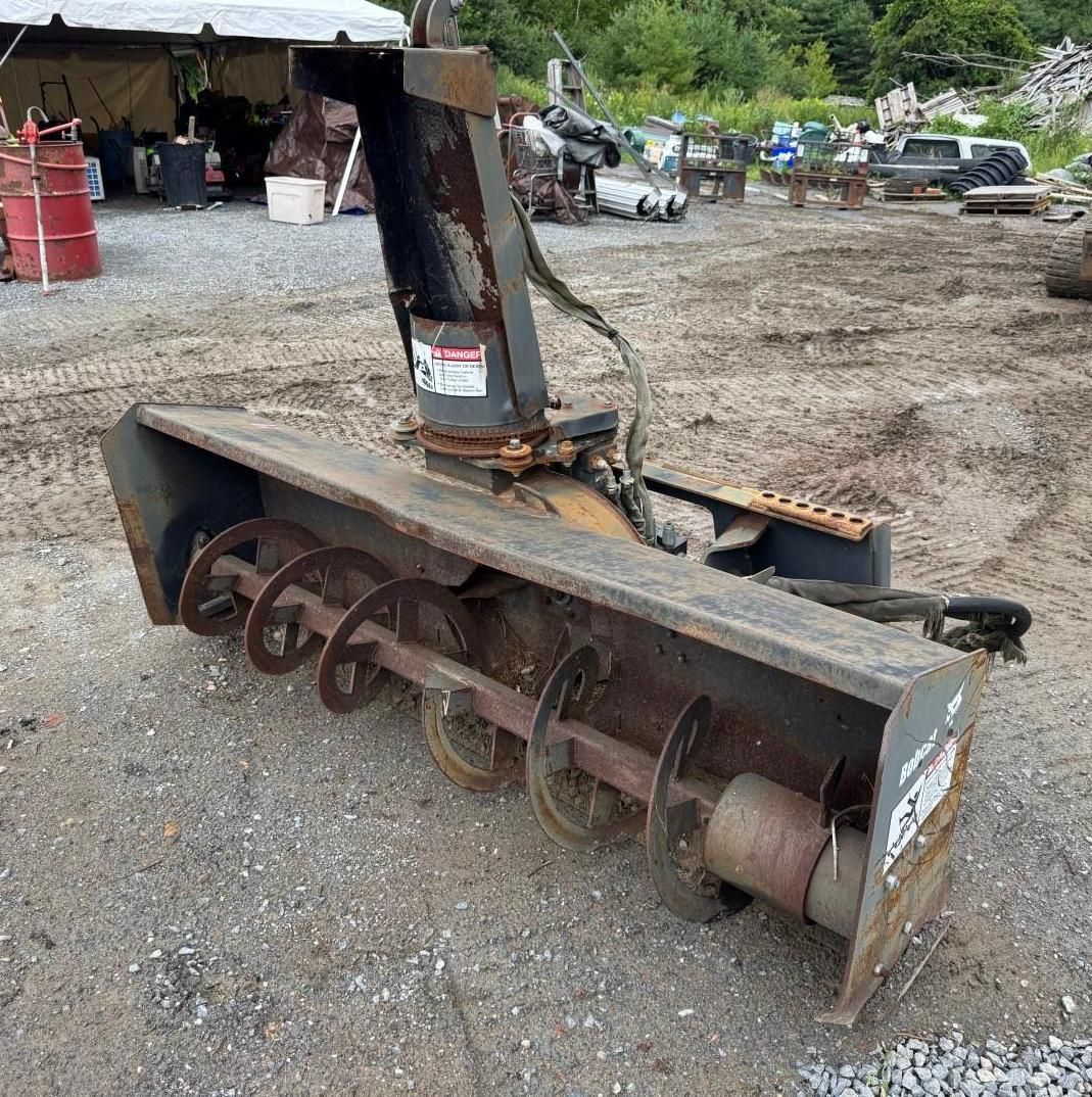 rotary snow blower attachment on gravel in an outdoor equipment yard.