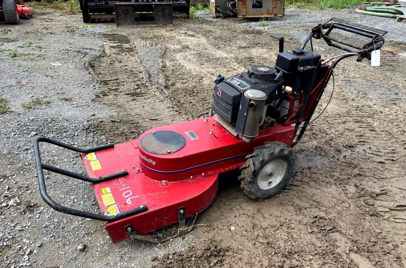 Red and black commercial mower on gravel, with front debris guard and large rear wheels.