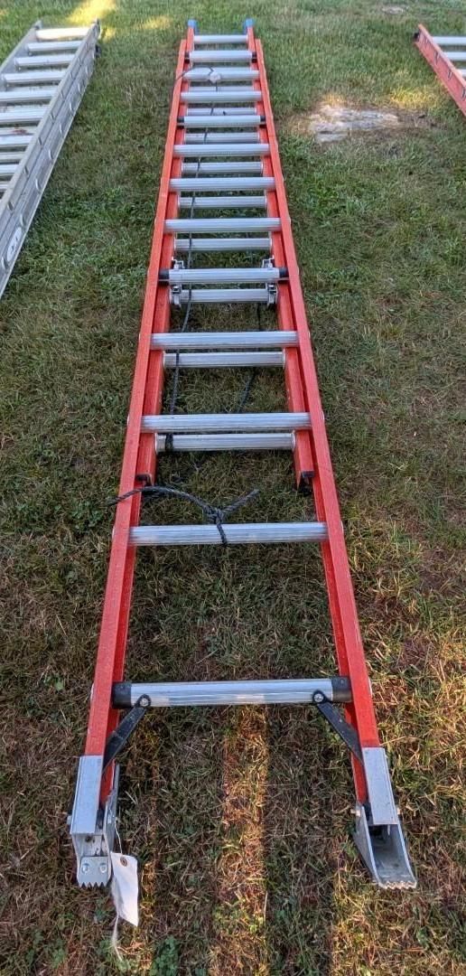 Red extension ladder lying on grass beside another ladder section.